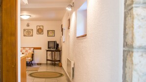 A hallway with a stone wall, a wooden door, and a tiled floor. There are framed pictures on the wall and a television on a stand. - Apartment Azur (Budva)