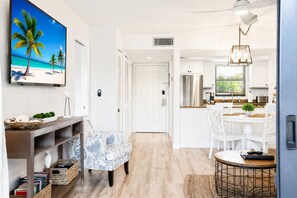A modern kitchen with white cabinetry, a dining area with a round table, and a living space with a patterned armchair.