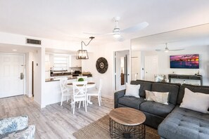 Ett modernt vardagsrum med en grå soffa, ett runt soffbord och en matplats med vita stolar.