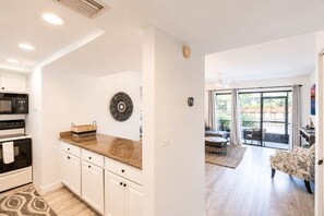 A modern kitchen with white cabinetry, a granite countertop, and a decorative wall piece. - Park Shore Resort-Deluxe Condo 1st FloorBLDGE #134 (Park Shore Resort)