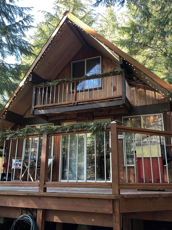 A wooden cabin with a balcony, large windows, and a sign welcoming visitors.