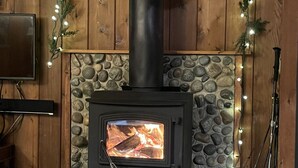 A stone fireplace with a black chimney, surrounded by a stone base, and decorated with Christmas stockings and lights.