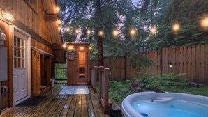 A wooden cabin with a hot tub, a deck, and a small cabin entrance.