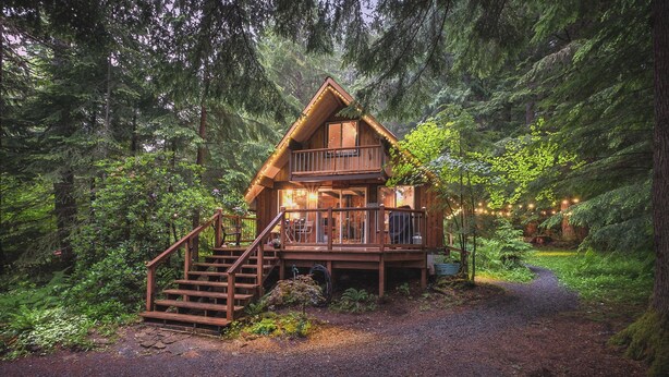 A cabin with a balcony, wooden stairs, and a gravel path leading to it.