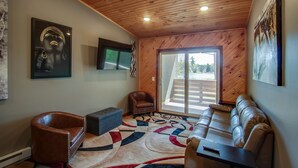 A modern living room with a wooden ceiling, a large sofa, a leather armchair, a coffee table, and a TV mounted on the wall. - Privat Hot Tub! Sleeps 6 *Traverse City *Sleeping Bear Dunes (Interlochen)