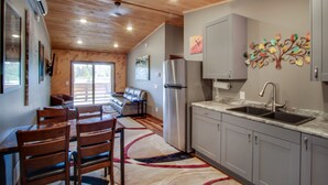A modern kitchen with grey cabinets, a stainless steel refrigerator, and a sink. There is a dining area with wooden chairs and a rug. - Privat Hot Tub! Sleeps 6 *Traverse City *Sleeping Bear Dunes (Interlochen)