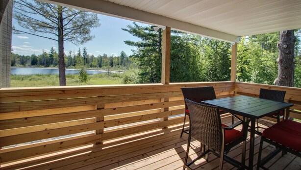 A wooden deck with a table and chairs, overlooking a lake and forest. - Privat Hot Tub! Sleeps 6 *Traverse City *Sleeping Bear Dunes (Interlochen)