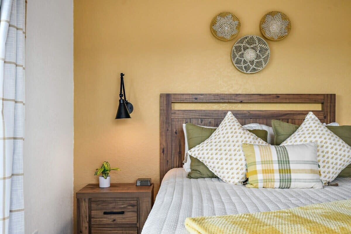 A bedroom with a wooden headboard, a bedside table with a plant, and decorative wall art.