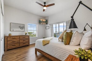 Quarto com cama, ventilador de teto, escrivaninha e janela com persianas.