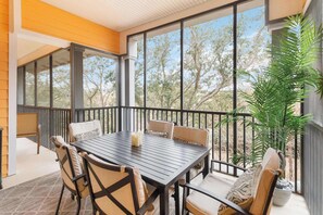 Eine überdachte Terrasse mit Tisch, Stühlen und einem Blumentopf, mit Blick auf Bäume.