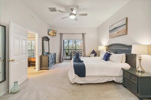 Ein Schlafzimmer mit Bett, Nachttischen, Kommode, Deckenventilator, Fenster mit Vorhängen und einer Tür.