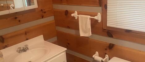Une salle de bain avec des murs en bois, un lavabo blanc, des toilettes et un miroir.