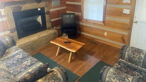 A cozy cabin interior with a stone fireplace, wooden walls, a television, and patterned furniture. - Beautiful Cabin Nestled in the Smokies (Hartford)
