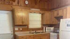 A wooden kitchen with a sink, stove, microwave, and refrigerator. There is a dining table with chairs and a window with blinds. - Beautiful Cabin Nestled in the Smokies (Hartford)