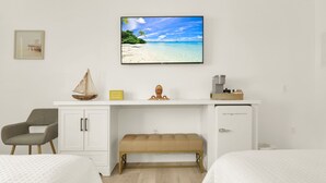A hotel room with a bed, a desk with a television displaying a beach scene, a chair, and a small cabinet. - Boutique Hotel 2 double beds with POOL, LOCATION! 1 block to BEACH/Restaurants (Deerfield Beach)