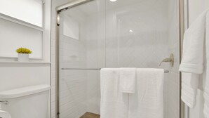 A modern bathroom with a glass shower enclosure, white tiles, and a wooden floor. - Boutique Hotel 2 double beds with POOL, LOCATION! 1 block to BEACH/Restaurants (Deerfield Beach)