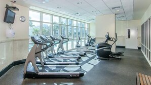 Un gimnasio con cintas de correr y una máquina elíptica, ventanas amplias y un reloj en la pared.