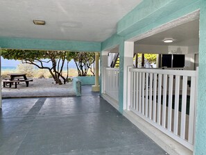 Relax in a covered outdoor space with a beach view, featuring a seating area and picnic tables.