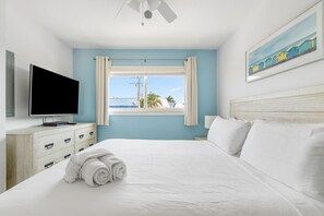 Une chambre d’hôtel comprenant un lit, un téléviseur à écran plat, une fenêtre avec des rideaux, un tableau et un ventilateur de plafond.