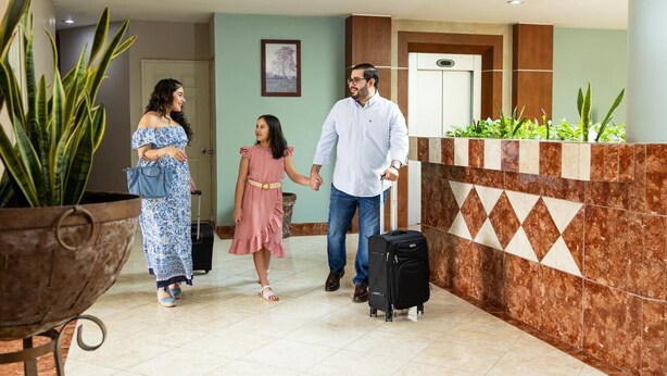 A reception area with a marble wall, a potted plant, and a piece of wall art. - Hotel San Juan (Villahermosa)