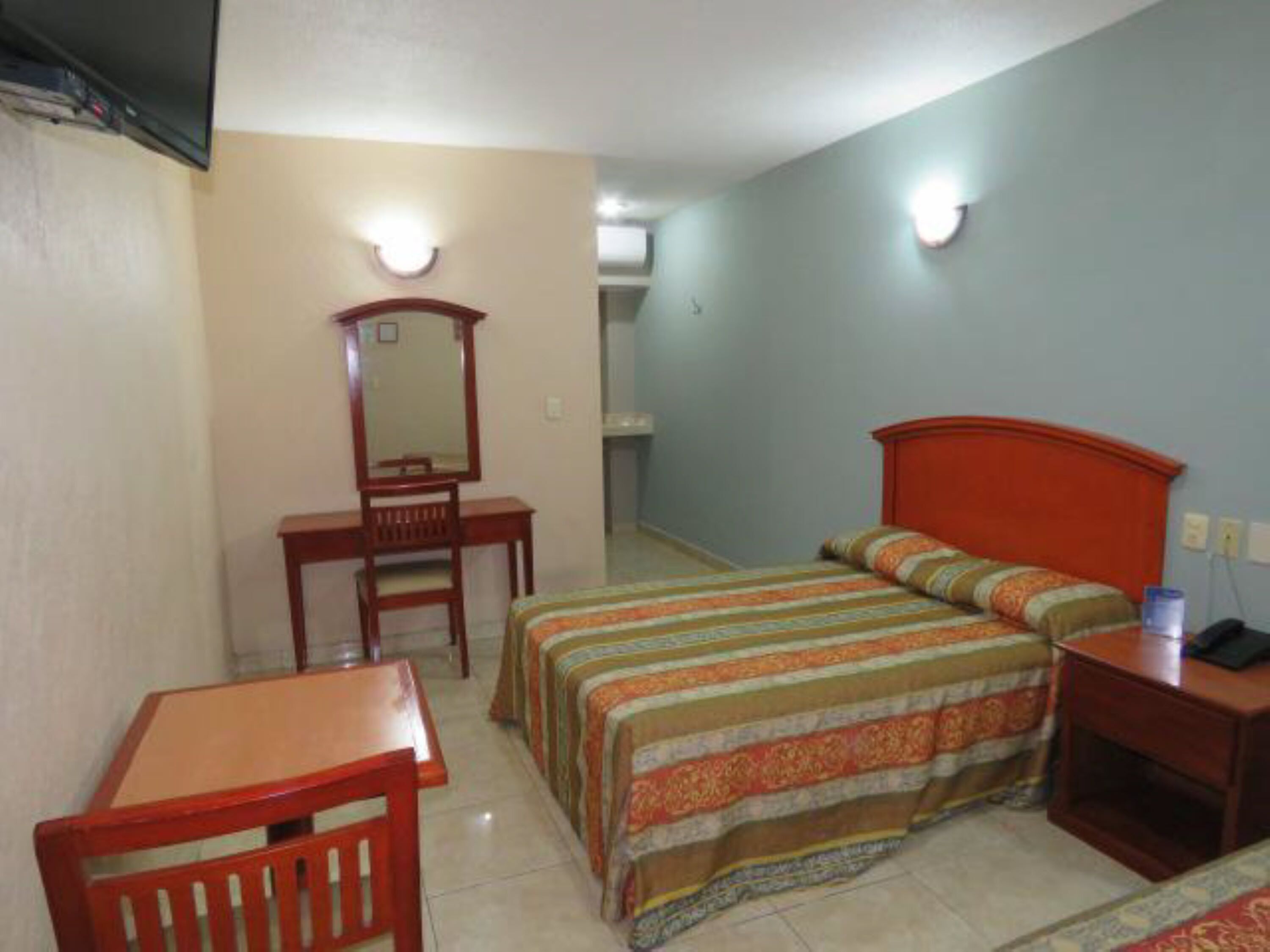 Un dormitorio con cama, escritorio, silla y espejo.