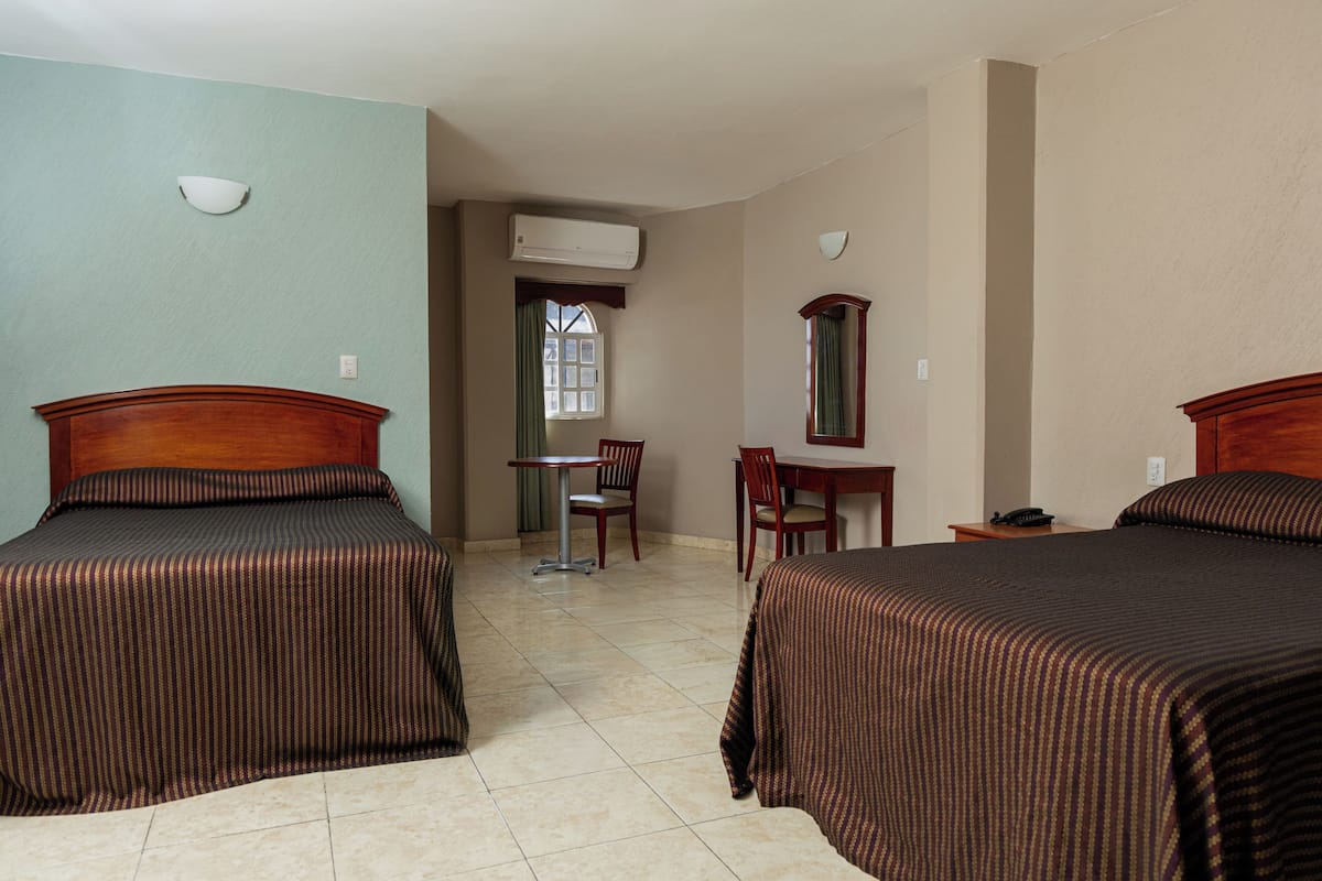 Habitación de hotel con dos camas, un escritorio, una silla, un espejo y un equipo de aire acondicionado.