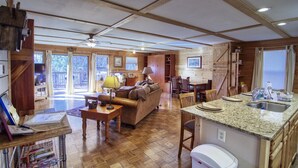 A cozy cabin interior with a wooden floor, a sofa, a dining area, and a kitchen with a granite countertop. - Secluded Cabin w/ HOT TUB, Woodburning Stove, VIEW on PRIVATE 2 acres (Cosby)