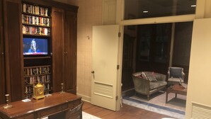 A hotel room with a wooden desk, a bookshelf, a television, a chair, and a view through a sliding door. - The Law Building (Natchez)