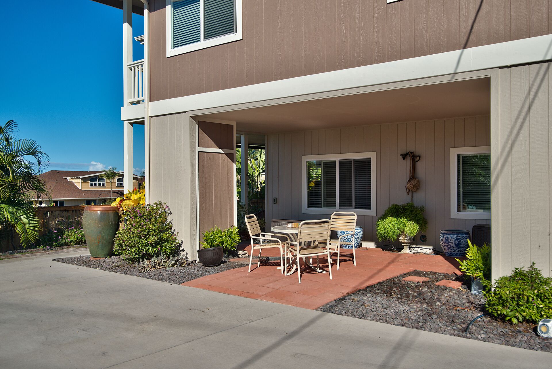 A patio with a table and chairs, surrounded by potted plants and a concrete walkway.