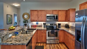 A modern kitchen with wooden cabinets, stainless steel appliances, granite countertops, and a built-in oven. - Kimo's Getaway (Kailua-Kona)