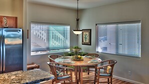 A dining area with a wooden table and chairs, a hanging light fixture, and large windows with blinds. - Kimo's Getaway (Kailua-Kona)