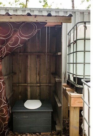 A compact, rustic toilet structure with a simple toilet seat and wooden platform, surrounded by a wooden fence.