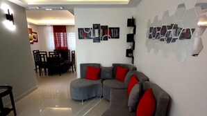A modern living room with a curved grey sofa, red cushions, and a dining area with a red curtain.
