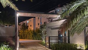 A gated entrance with a covered walkway, palm trees, and buildings in the background.