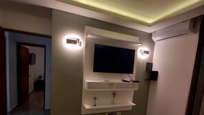A modern bedroom with a flat-screen TV mounted on a wall, a bedside table, and a built-in air conditioning unit.