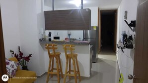 A compact kitchen with a built-in refrigerator, a wooden island with stools, and a white wall with a door on the right.