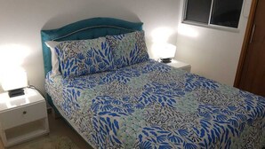 A bed with a blue and white floral bedspread, two bedside lamps, and a white nightstand.