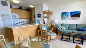 A compact living space with a kitchenette, a dining area with a glass table, and a seating area with a sofa and chairs. - Spectacular Summer Specials - Beachfront Condo With Amazing Oceanfront Views. (Kihei)