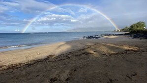 A beach with a rainbow, calm sea, and distant buildings. - Spectacular Summer Specials - Beachfront Condo With Amazing Oceanfront Views. (Kihei)