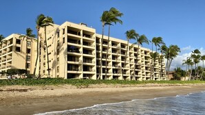 A beachfront hotel with multiple floors, palm trees, and a sandy beach. - Spectacular Summer Specials - Beachfront Condo With Amazing Oceanfront Views. (Kihei)