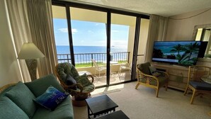 A living room with a sofa, armchairs, a coffee table, and a TV. The room has a view of the ocean through large sliding doors. - Spectacular Summer Specials - Beachfront Condo With Amazing Oceanfront Views. (Kihei)