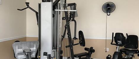 A gym with a variety of exercise equipment including a weight bench, a stationary bike, and a multi-functional workout machine.