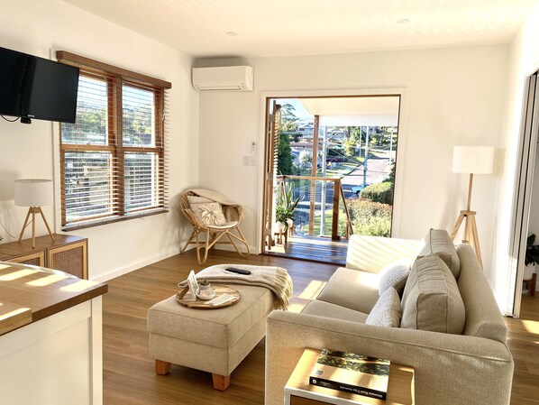 A modern living room with a sofa, ottoman, and a chair with a view through a glass door. - 1 Hour from Sydney 500 meters to Terrigal beach, restaurants and night life. (Terrigal)