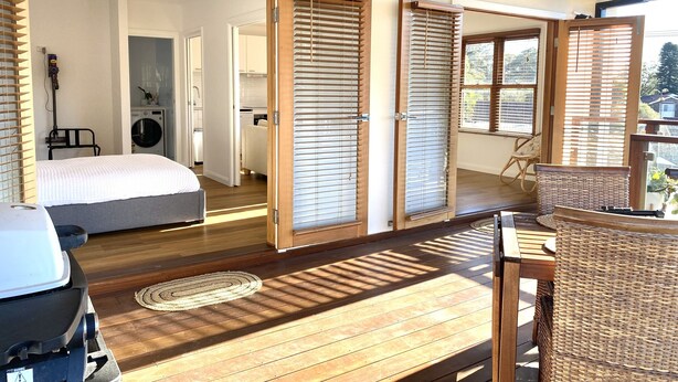 A modern, well-lit room with a bed, a dining area with a wicker chair, and a view of the outside. - 1 Hour from Sydney 500 meters to Terrigal beach, restaurants and night life. (Terrigal)