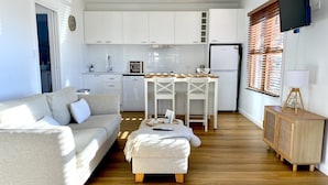 A compact living space with a sofa, a small dining table, a kitchenette, and a TV mounted on the wall. - 1 Hour from Sydney 500 meters to Terrigal beach, restaurants and night life. (Terrigal)