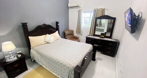 A bedroom with a bed, a chair, a dresser, a mirror, and an air conditioner.