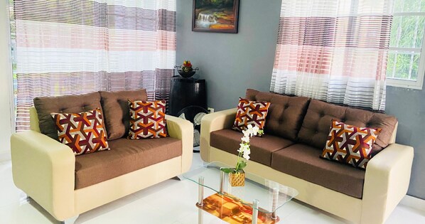 A living room with two sofas, patterned cushions, a glass coffee table, and a framed picture on the wall.