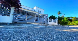 A modern building with a gated entrance, gravel driveway, and lush greenery.