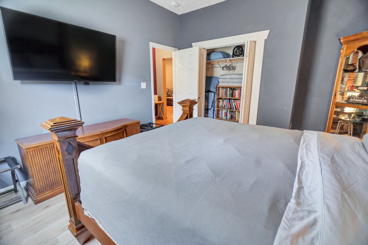 A bedroom with a large bed, a TV mounted on the wall, a wooden dresser, and a bookshelf.