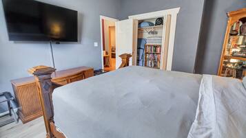 A bedroom with a large bed, a TV mounted on the wall, a wooden dresser, and a bookshelf.